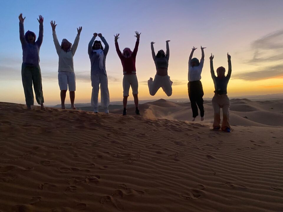 Camels trekking through the massive orange dunes of Erg Chebbi during sunset on a Marrakech to Fes desert tour